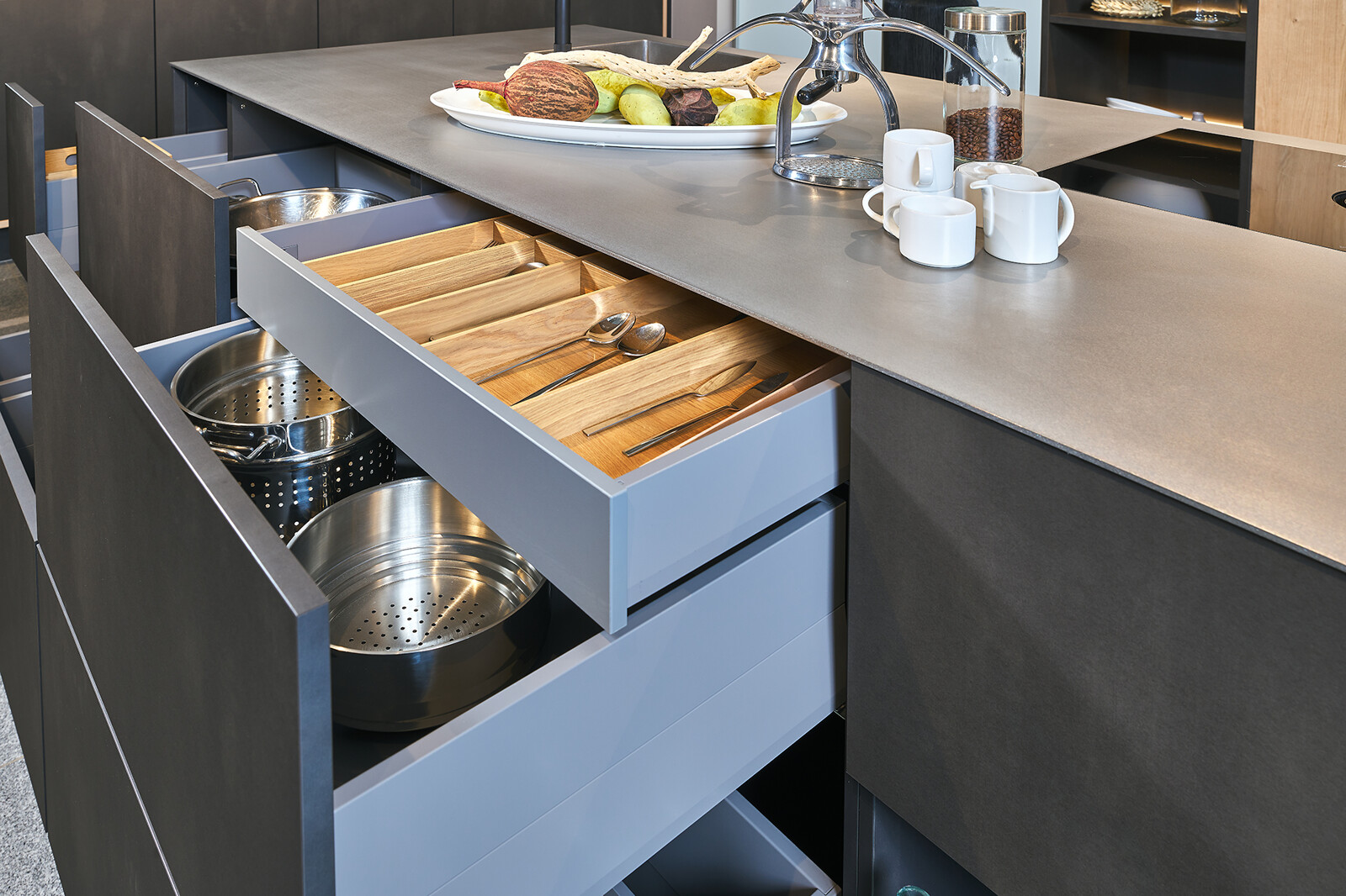 Showroomkeuken: Industriële eilandkeuken van Contur met rvs blad, staallook fronten, veel lades en houten ladeinrichting