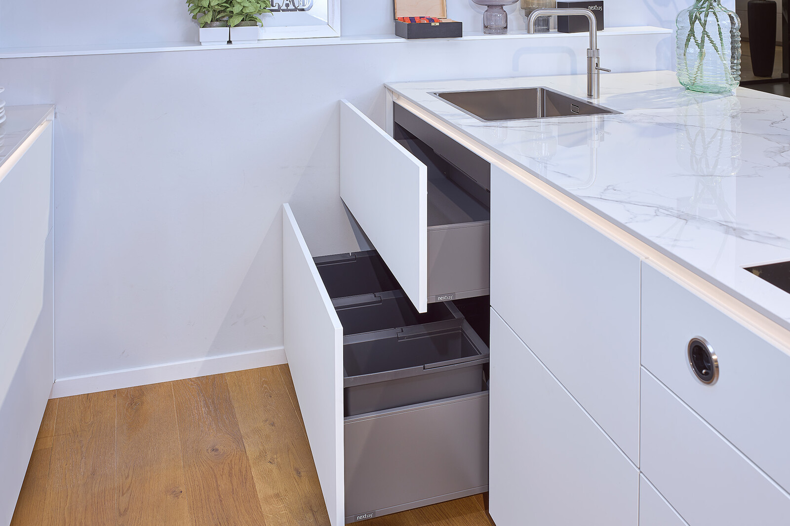 Showroomkeuken next125 - Witte eilandkeuken in fenix en notenhout met praktisch afvalsysteem