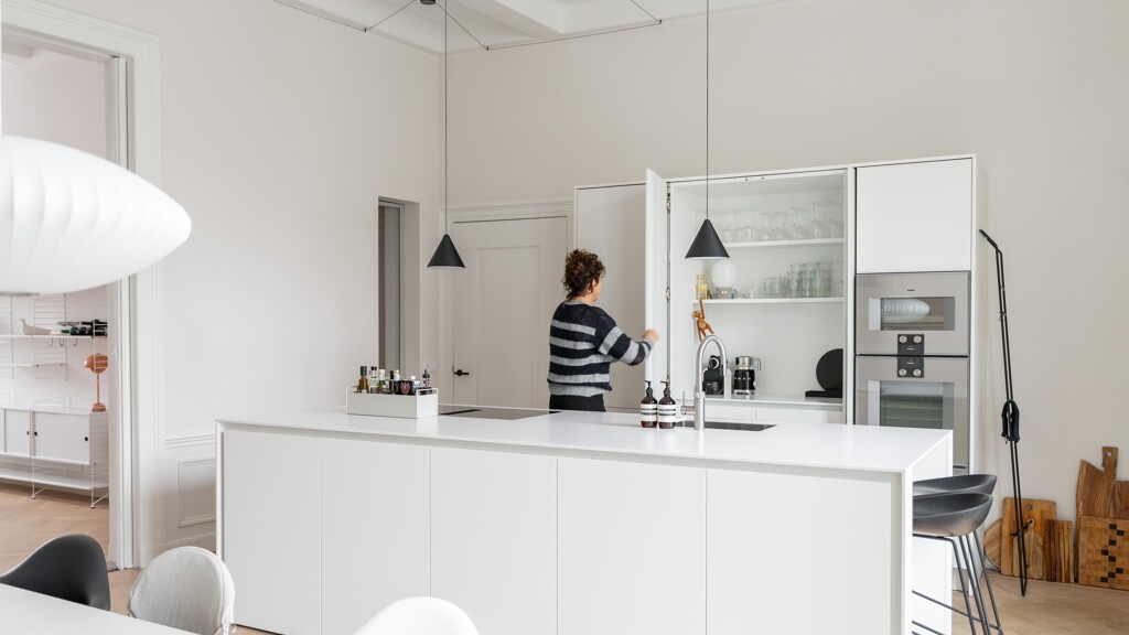 Een witte eilandkeuken met nis en pocket deuren. Mies Interieur, Charlotte Kap Fotografie