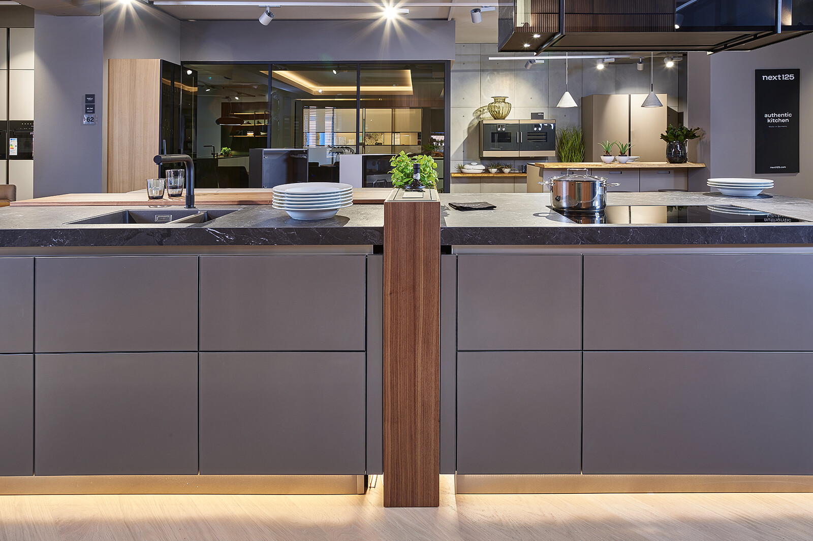 Showroomkeuken: next125 designkeuken met kookeiland in notenhout en matglas met plintverlichting 