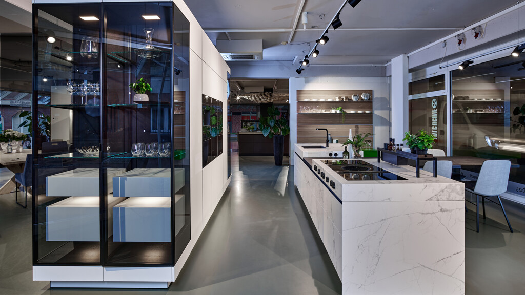 Prachtige SieMatic SLX Ceramic. Het keukeneiland heeft fronten, zijpanelen en een werkblad van keramiek met marmerdecor. De vrijstaande kastenwand heeft aan beide zijdes SLX vitrinekasten.