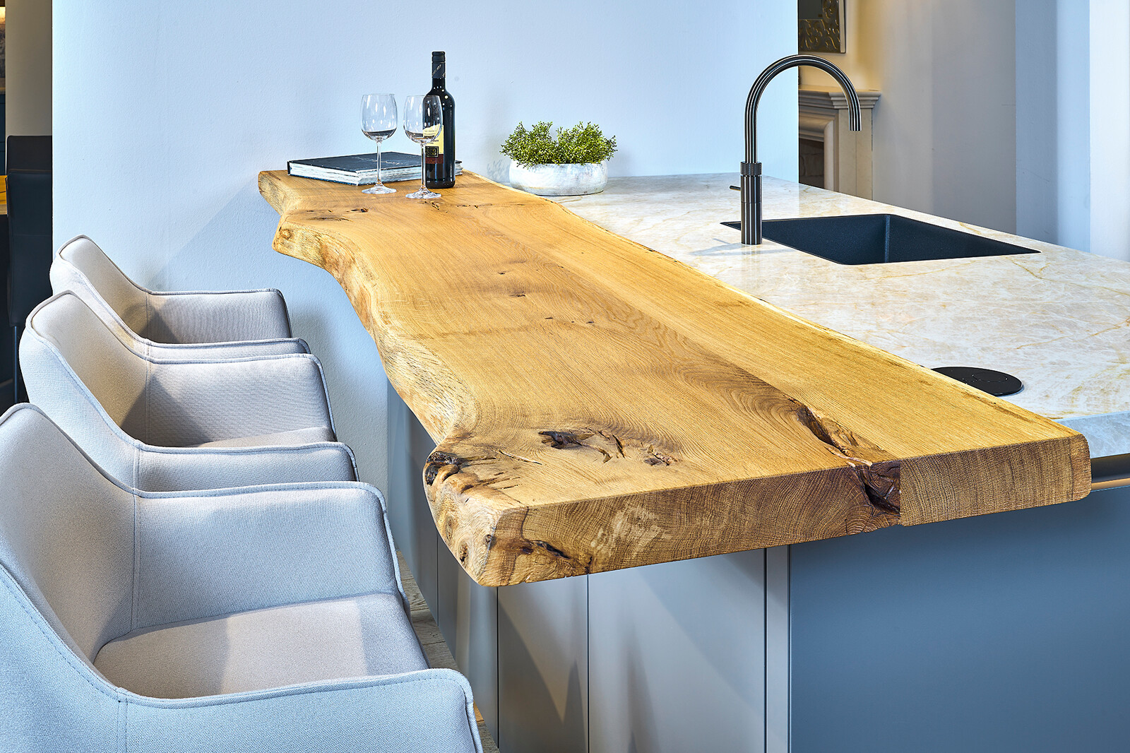 Showroomkeuken Ballerina: taupe eilandkeuken met houten bar met boomkant en glanzend keramiek blad