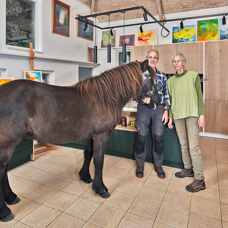 Landelijke groene keuken van Contur met matgroene fronten en fronten in licht eiken fineer. Het keukenblad is van Blue Sky graniet. Het paard van de zorgboerderij staat er speciaal voor onze fotograaf.