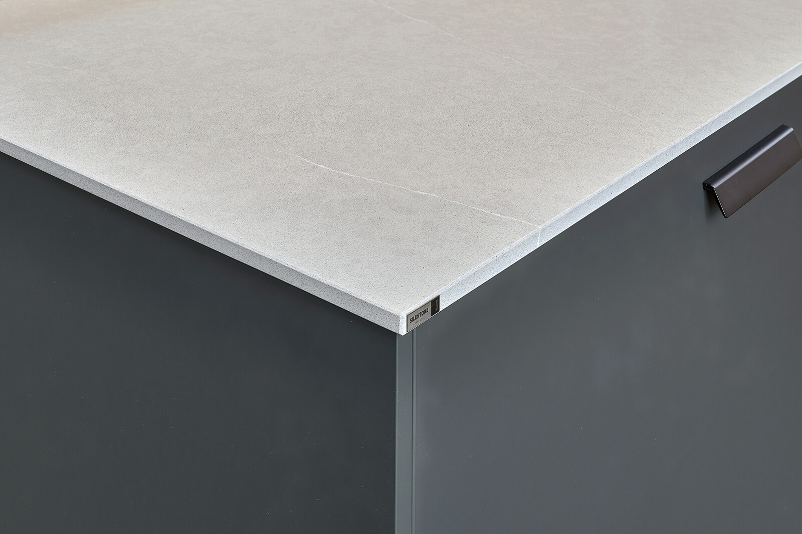 Showroomkeuken: Eilandkeuken met bar in lavazwart en eiken met wit composiet keukenblad.