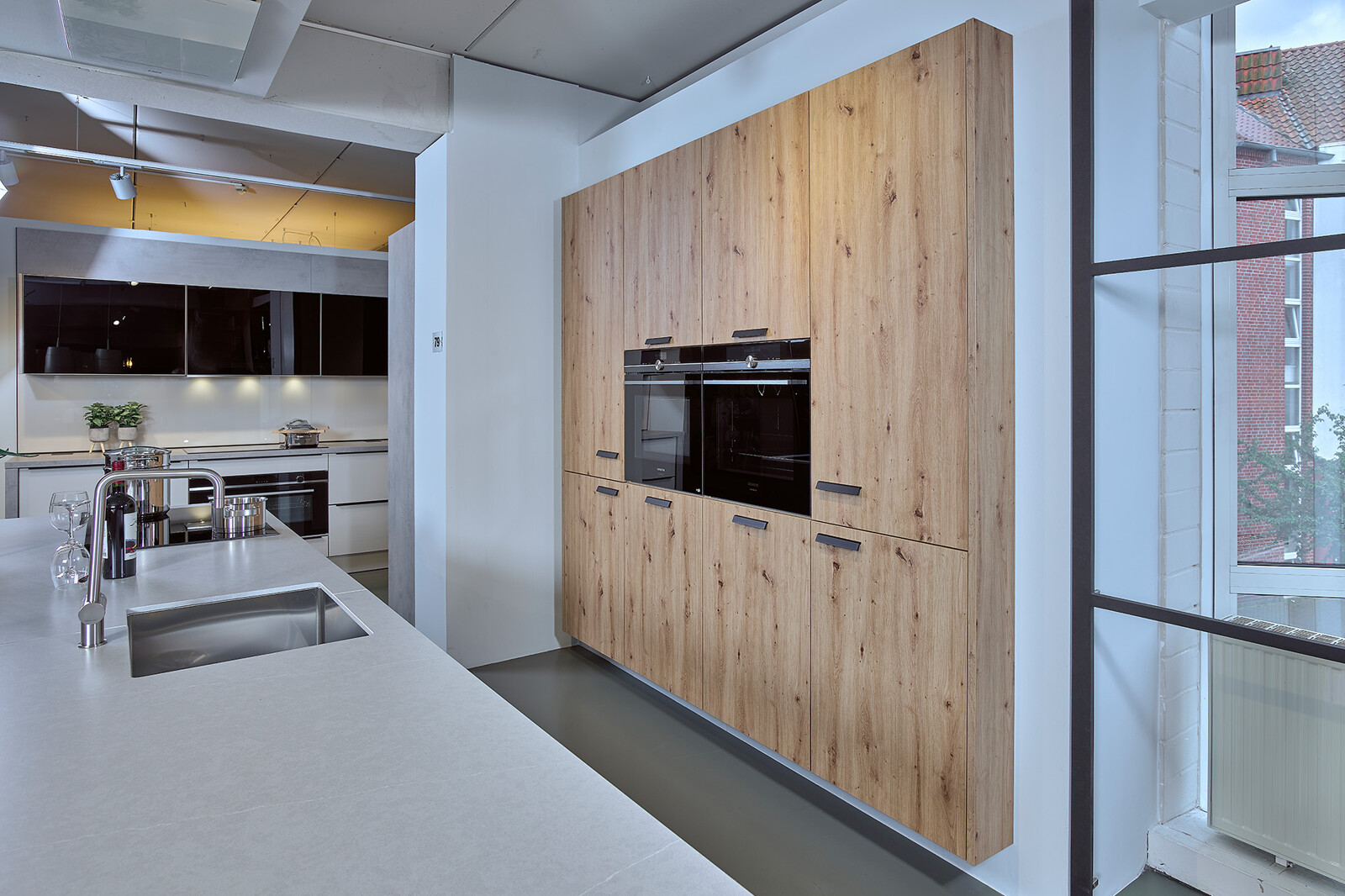 Showroomkeuken: Eilandkeuken in matzwart en eiken kastenwand met wit composiet aanrechtblad en Siemens apparatuur