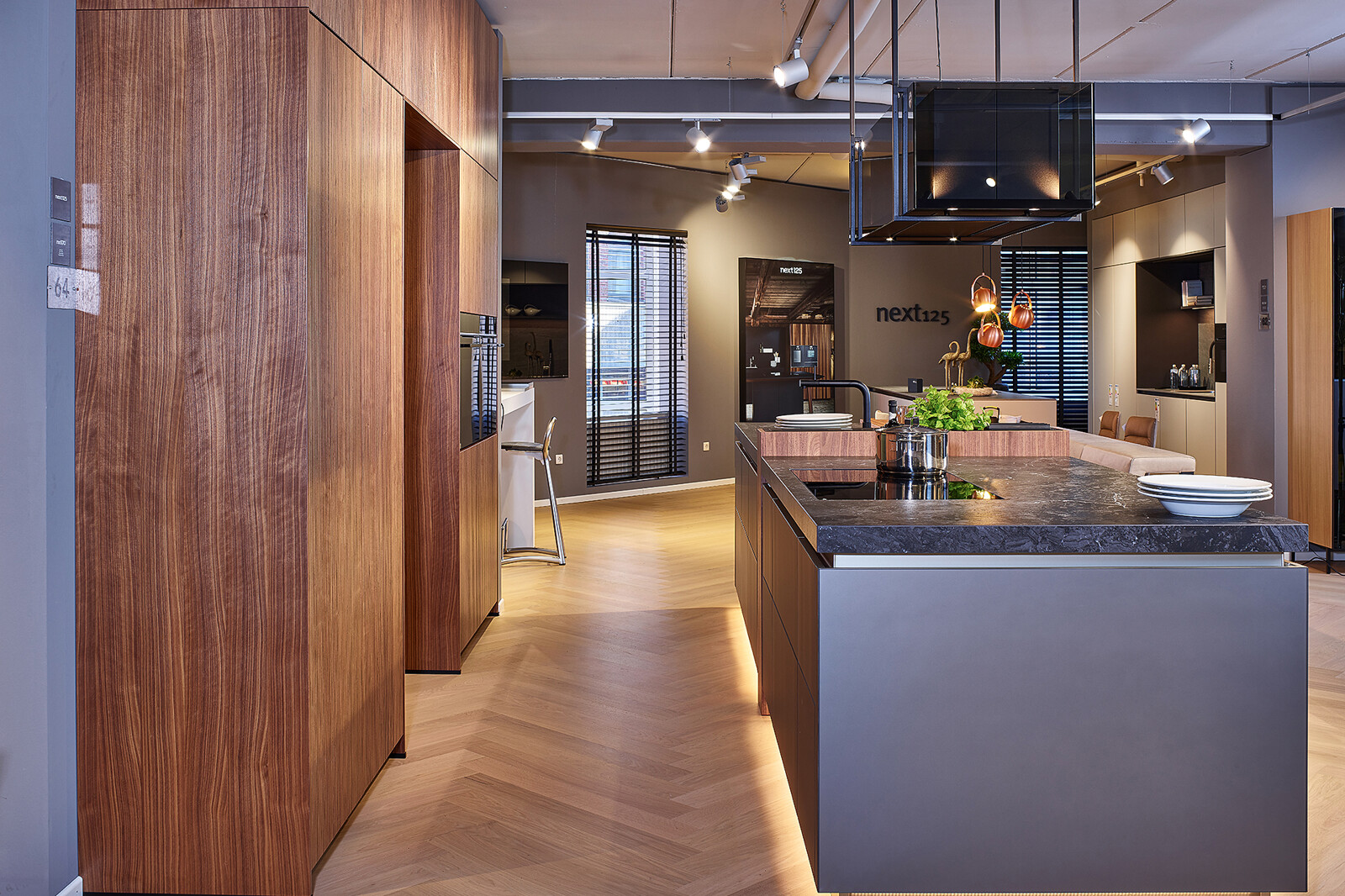 Showroomkeuken: next125 designkeuken met kookeiland in notenhout en matglas met plintverlichting onder het keukeneiland