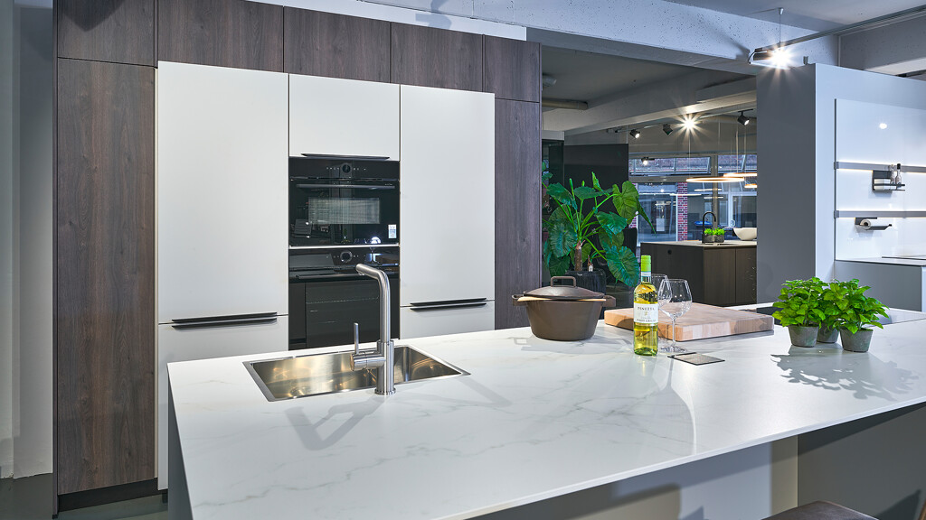 Stilvolle Inselküche in Kieselgrau und dunkler Eiche (Nachb.). Die Arbeitsplatte besteht aus Komposit in Marmoroptik, an der Insel ist Platz für zwei Barhocker.