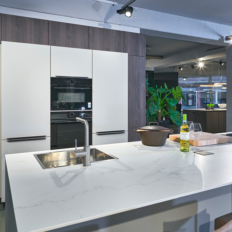 Stilvolle Inselküche in Kieselgrau und dunkler Eiche (Nachb.). Die Arbeitsplatte besteht aus Komposit in Marmoroptik, an der Insel ist Platz für zwei Barhocker.