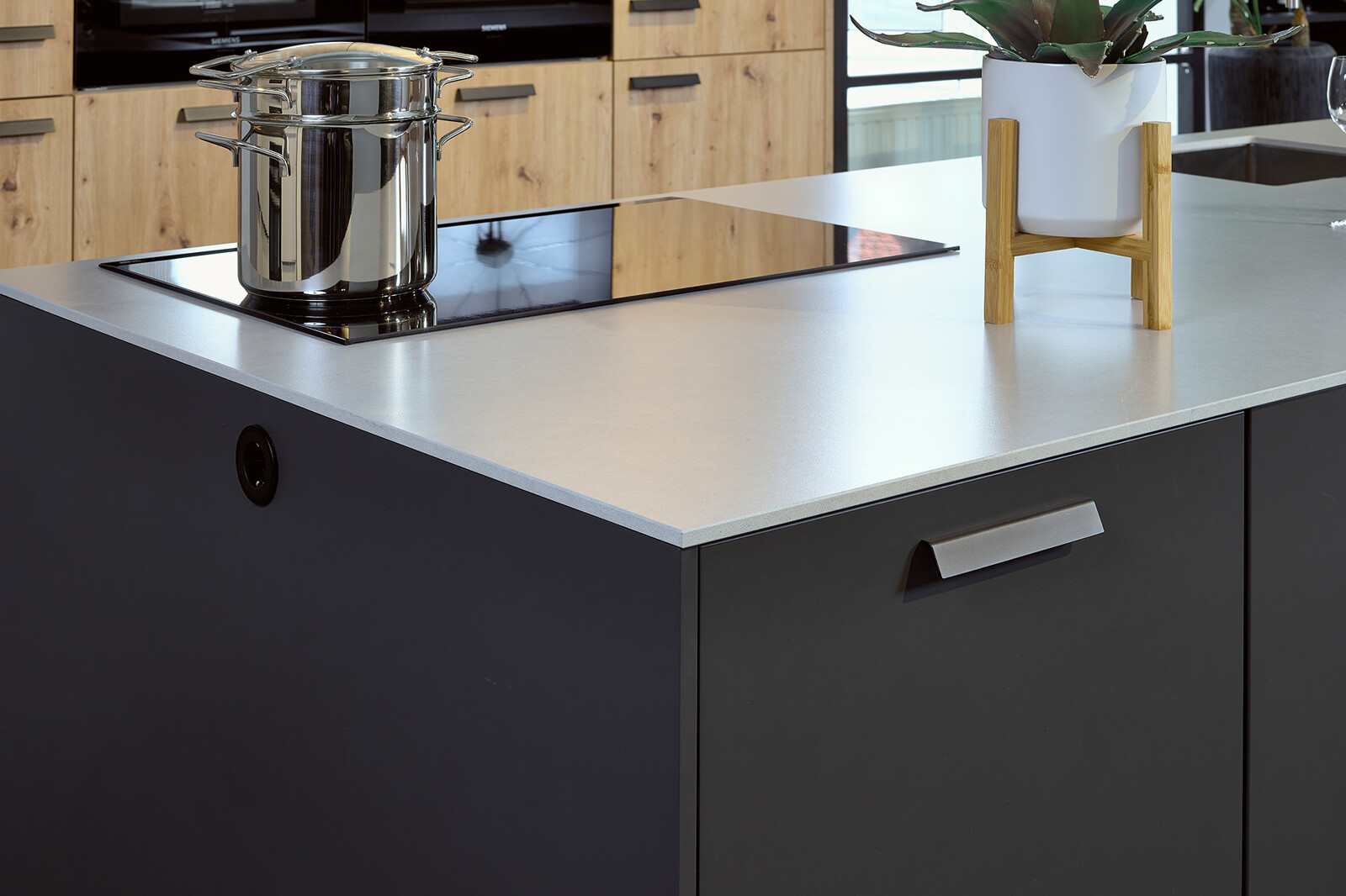 Showroomkeuken: Eilandkeuken met bar in matzwart en eikenlook met wit composiet aanrechtblad