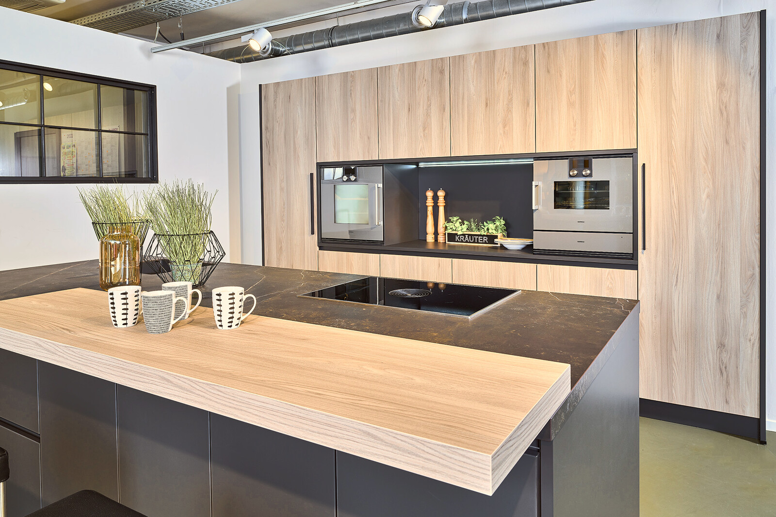 Showroomkeuken: Zwarte eilandkeuken met essen houten kastenwand en bar