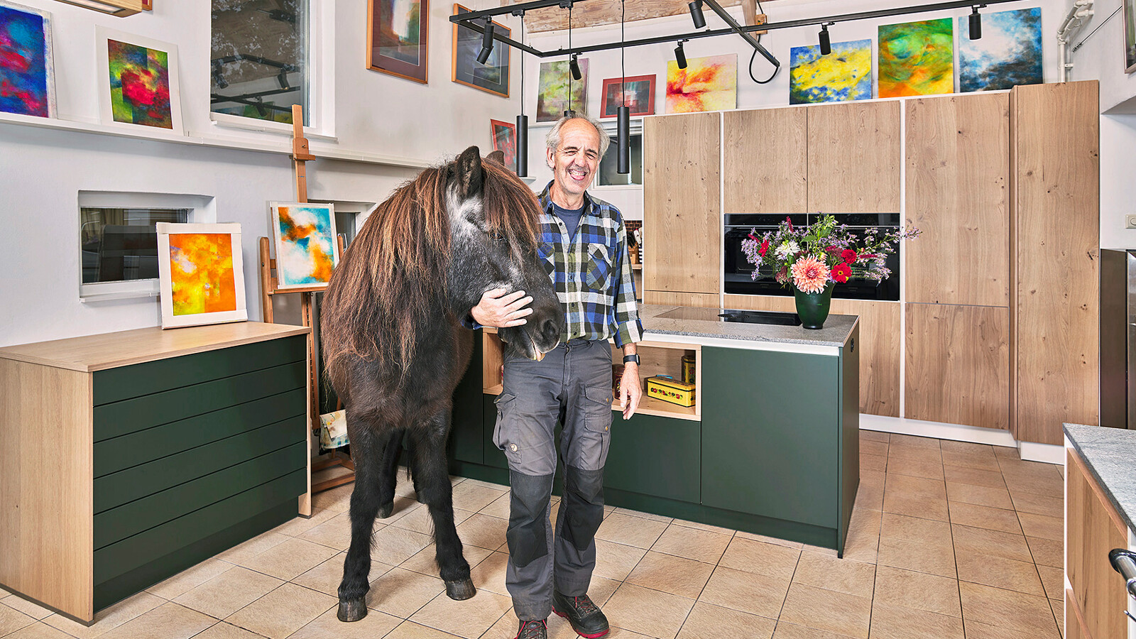 Groene landelijke keuken van Contur met matgroene fronten en fronten in licht eiken fineer. Het keukenblad is van Sky Blue graniet. Het paard van de zorgboerderij staat speciaal voor onze fotograaf in de keuken. 