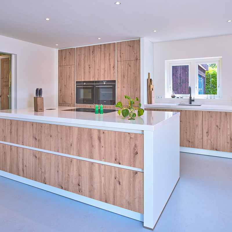 Skandinavische Küche. Inselküche in Eiche mit weißer Komposit-Arbeitsplatte und weißen Seitenwänden.