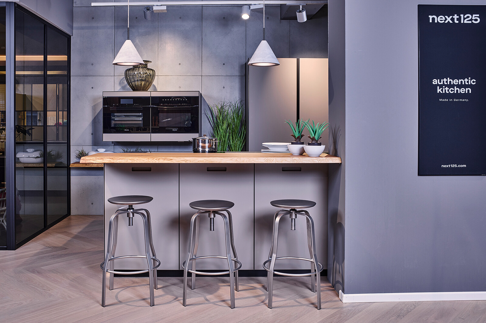 Showroomkeuken: next125 compacte industriële eilandkeuken met houten bar en matglas fronten