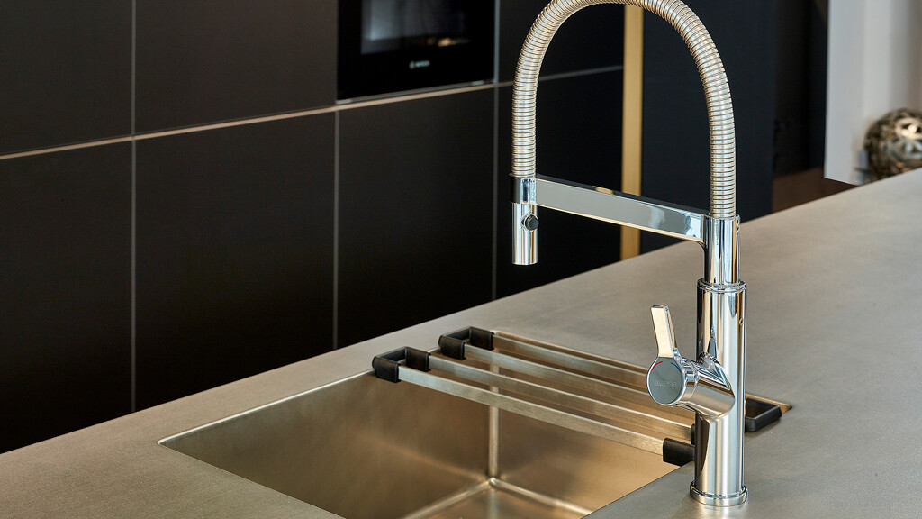 Schwarze Inselküche mit Edelstahl Arbeitsplatte und eingeschweißter Spüle. Die Küche ist von next125 | Ekelhoff Küchen, Nordhorn