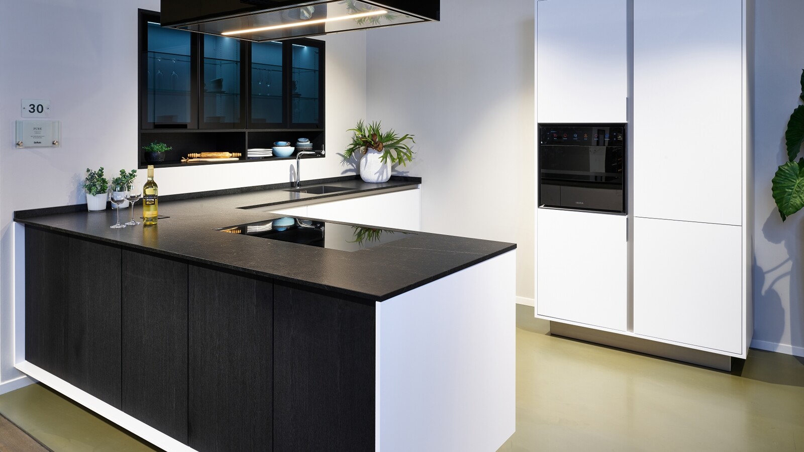 In de Ekelhoff  keukenshowroom in Nordhorn vindt u deze hoekkeuken met schiereiland van SieMatic, uit de Mondial lijn. In zwart Eiken Darjeeling en Lotuswitte Similaque. Met een granieten keukenblad en ingebouwde bovenkasten.