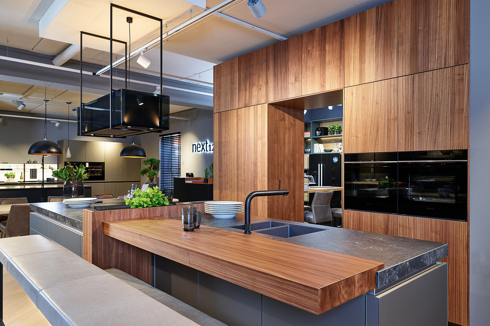 Showroomkeuken: next125 designkeuken met kookeiland in notenhout en matglas met houten bar