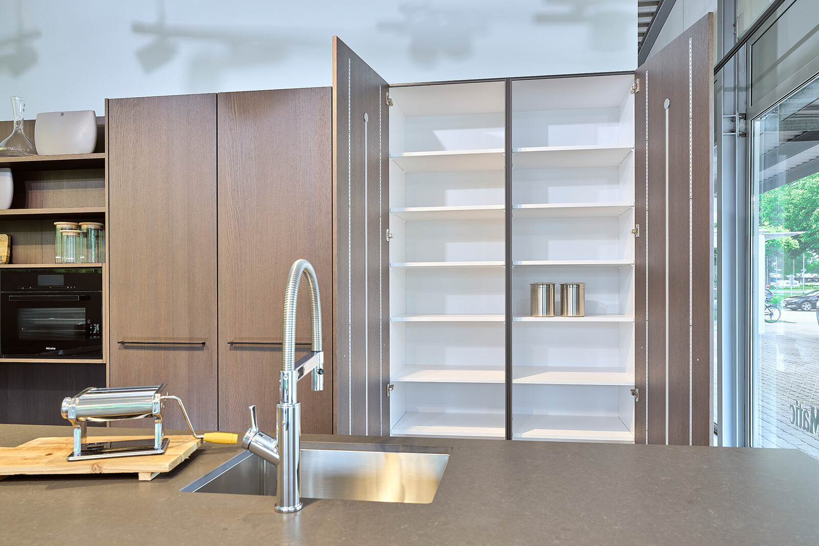 Showroomkeuken: SieMatic designkeuken met eiland in lichtgrijze similaque en hoge kasten in eikenfineer