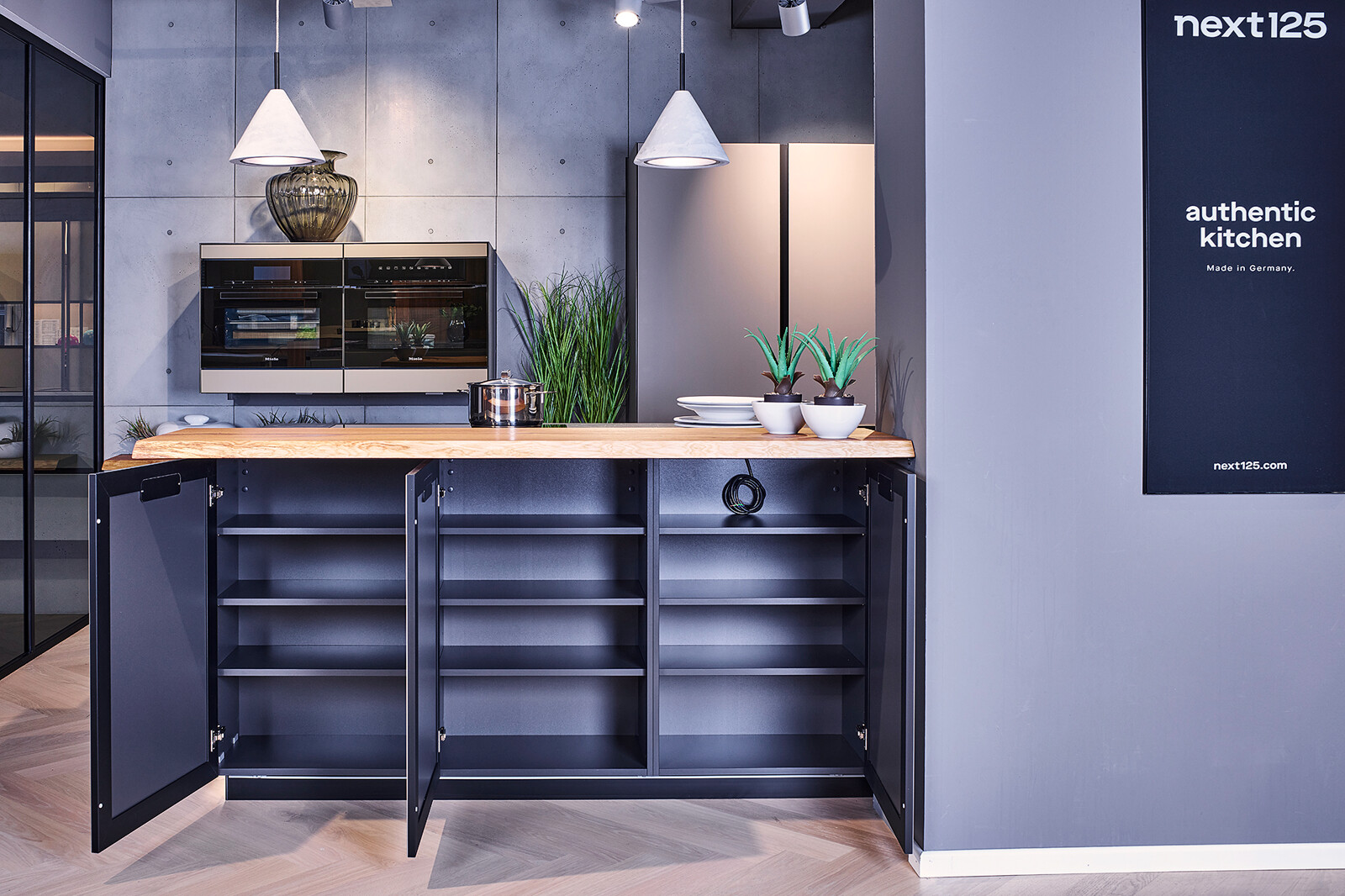 Showroomkeuken: next125 industriële eilandkeuken met keramisch aanrechtblad Somnia houten bar en zwart corpus