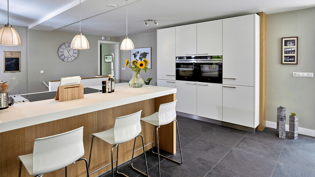 Keuken met schiereiland en hoge kast in wit en licht eiken met wit composiet keukenblad. Van Ekelhoff Kuchen, Nordhorn