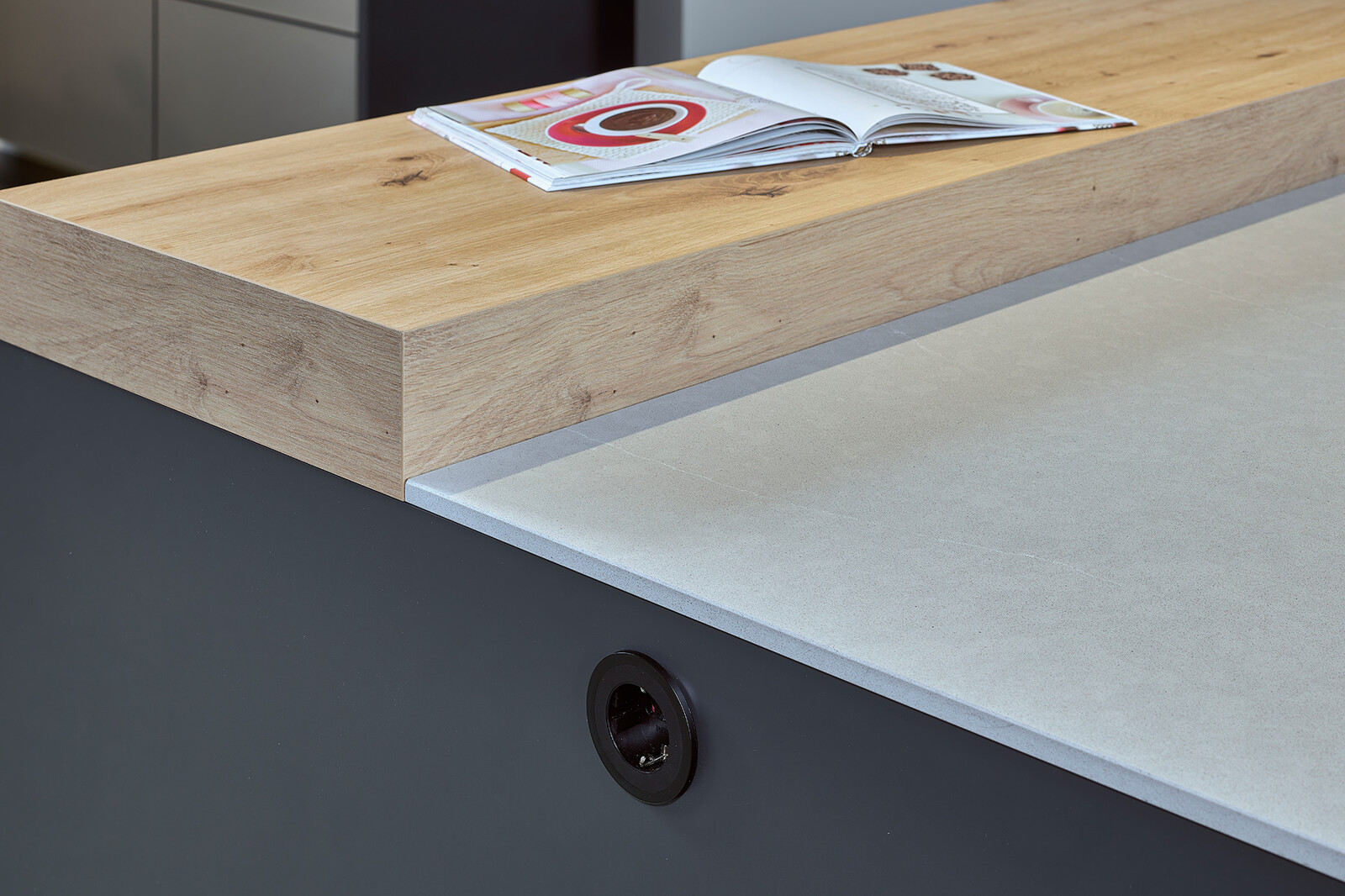 Showroomkeuken: Eilandkeuken met bar in matzwart en eiken met wit composiet keukenblad.