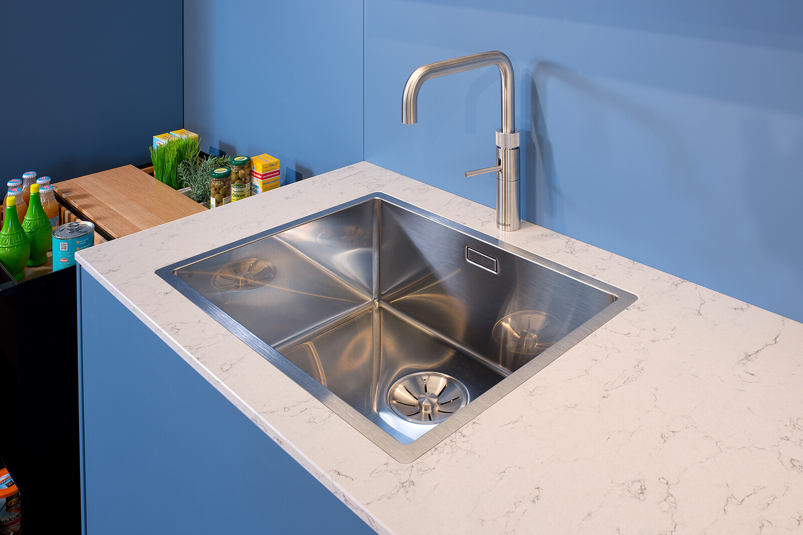 Showroomkeuken: next125 Blauwe designkeuken met wit composiet werkblad en quooker kraan