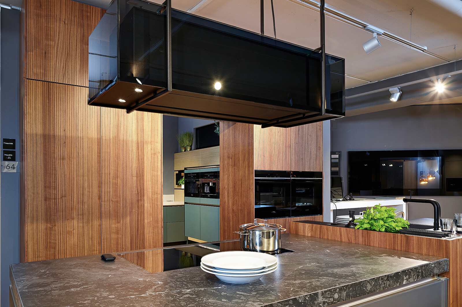 Showroomkeuken: next125 designkeuken met kookeiland in notenhout en matglas met design afzuigkap