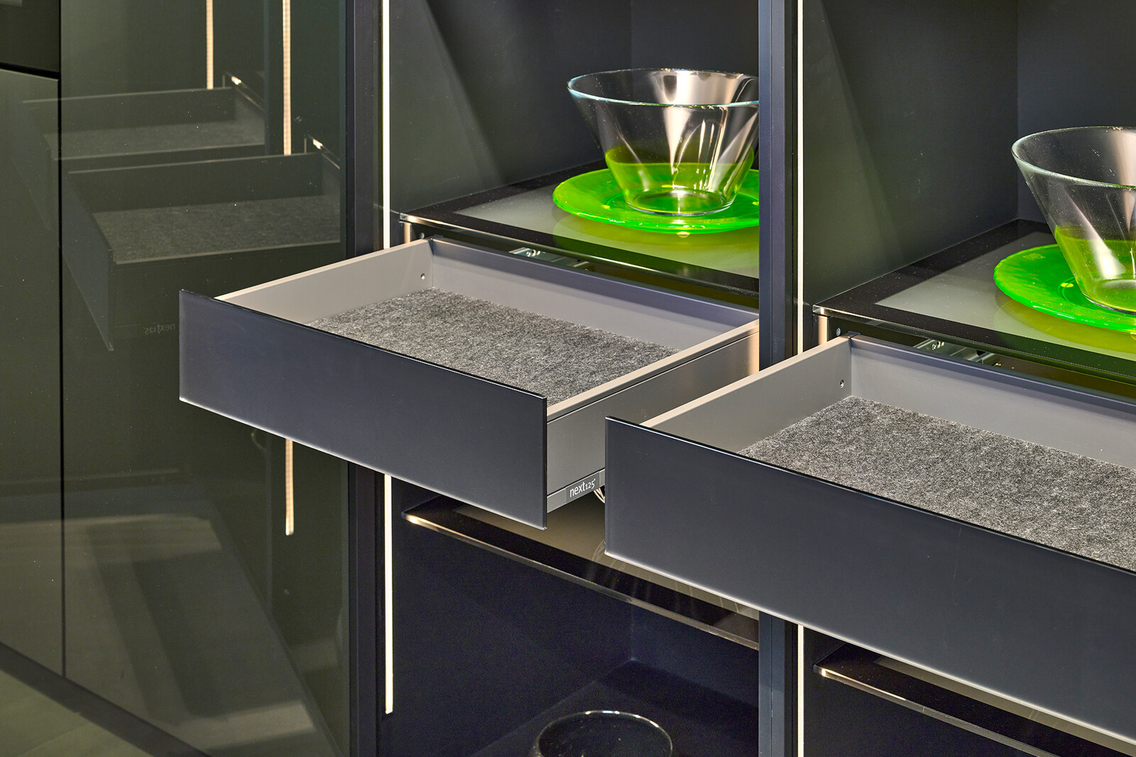 Showroomkeuken: next125 designkeuken in metallic Inox SensiQ en vitrinekast met zwarte glasdeuren en binnenlades