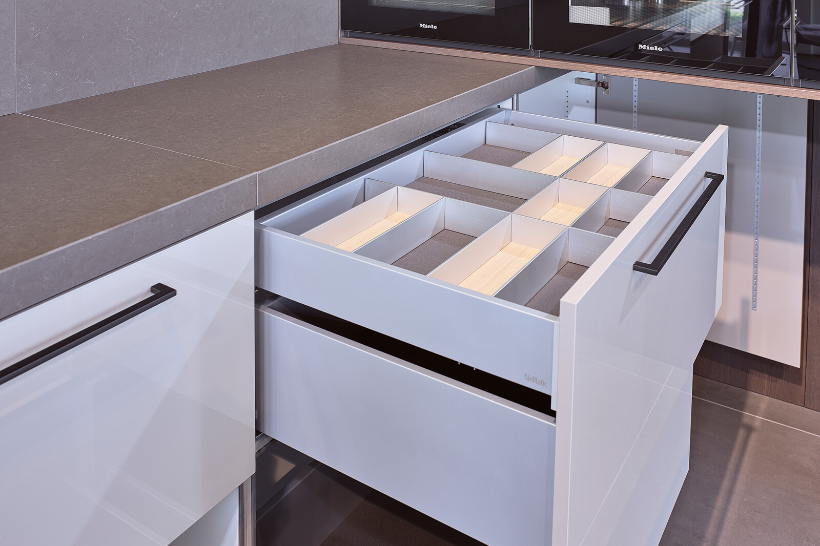 Showroomkeuken: SieMatic designkeuken in L-vorm met keukeneiland in lichtgrijs en eiken  met  lades en binnenlades