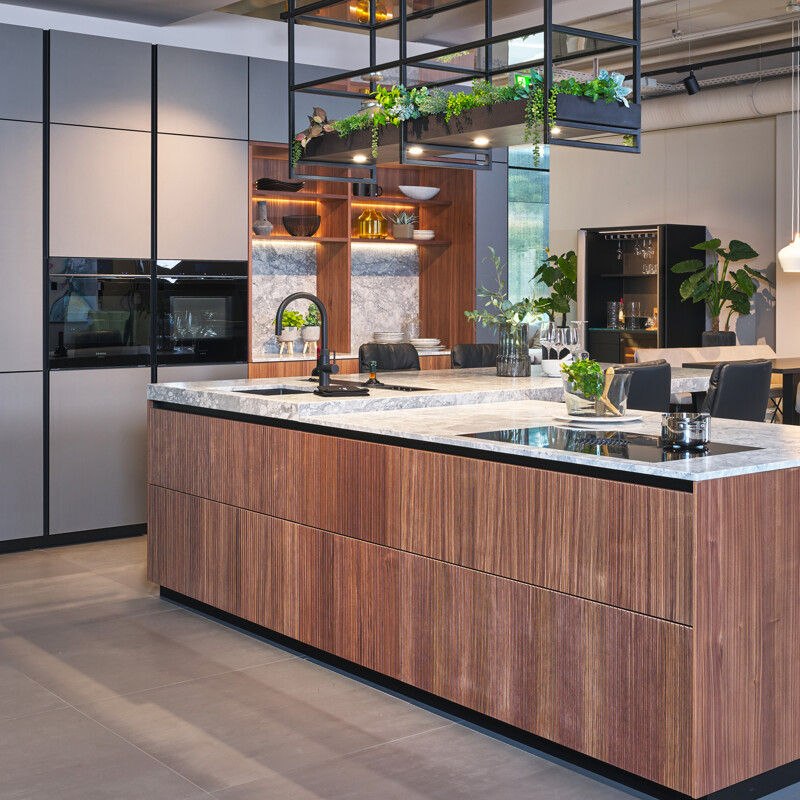 Außergewöhnliche Inselküche von next125 mit geriffelten Fronten in Nussbaum und einem Hochschrank mit Mattglasfronten in Basaltgrau. Mit Küchenarbeitsplatte aus Granit in der Ausführung Superwhite. Zu sehen beim Küchenland Ekelhoff in Nordhorn