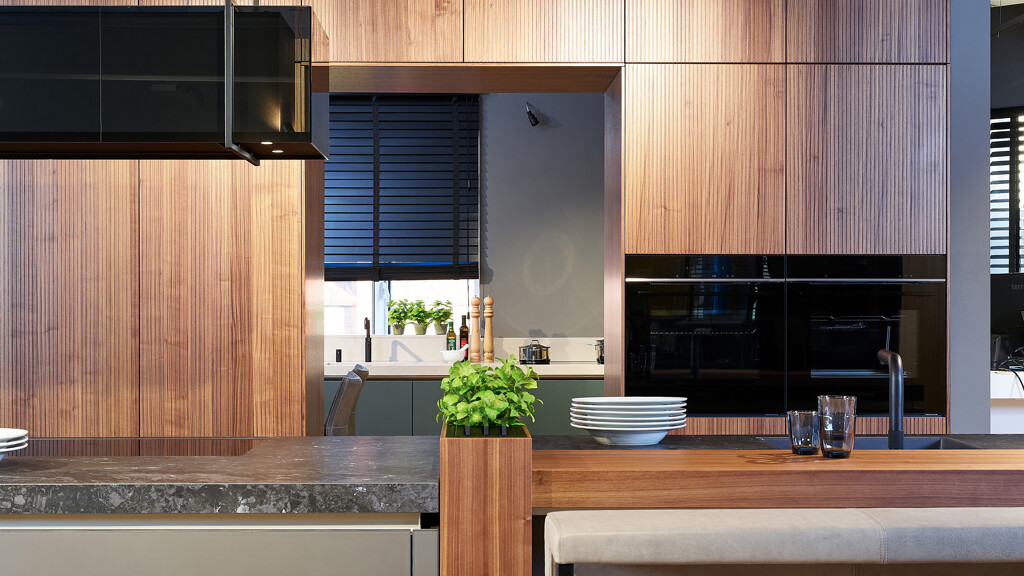 Grote eilandkeuken met doorgang in de astenwand. Fronten zijn van notenhout met groeven of ribbels. Te zien bij Ekelhoff Keukens  in Nordhorn.